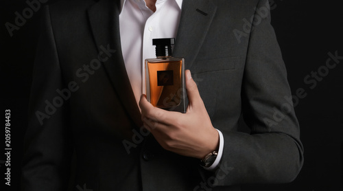 Man in formal suit holds glass perfume bottle. Elegant businessman shows luxury fragrance. Gentleman offers cologne for personal care and style.