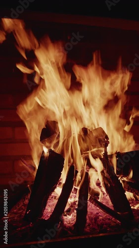 A cozy burning bonfire with bright orange flames and glowing logs inside a brick fireplace or barbecue area.
