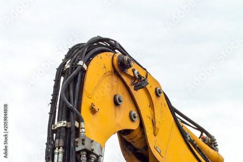 Fotografie Yellow excavator arm with hydraulic hoses against cloudy sky construction and re