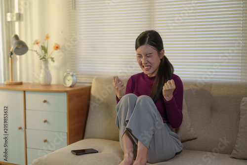 Cuadro en lienzo Young woman sitting on a sofa, expressing strong anger and frustration while cle