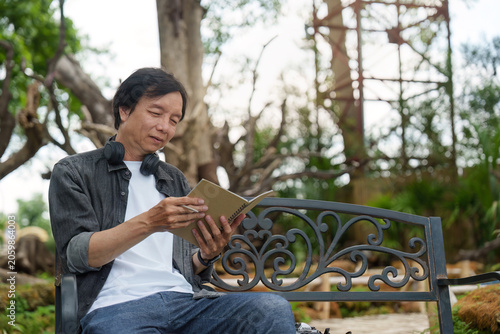 Fotografía Asian senior man reading notebook on park bench for lifelong learning and active