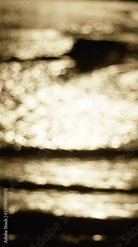 A stunning 4K slow motion abstract background featuring shimmering golden bokeh on a water surface during sunset. The out-of-focus light circles create a dreamy, peaceful, and ethereal atmosphere.