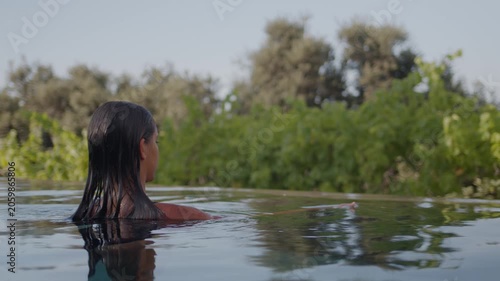 Young girl emerges from the pool, relaxing and enjoying the beautiful view of nature.