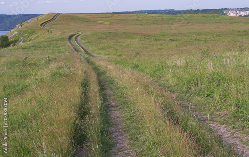 Quiet dirt roads winding across grassy hills and wildflower meadows, creating a peaceful setting for road trips, outdoor adventures and nature tourism.