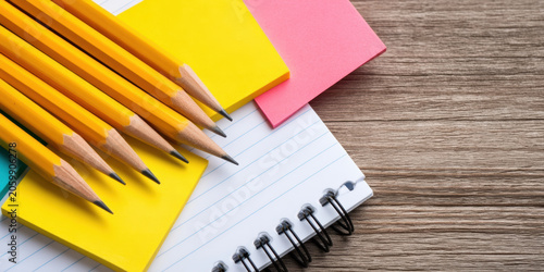 Yellow pencils are neatly arranged on colorful sticky notes beside a spiral notebook on a wooden surface.