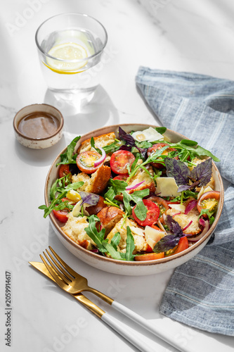 Tuscan panzanella salad with tomatoes, red onion, arugula, basil, cheese and bread in a bowl