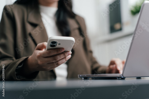 Fotografie Businesswoman holding smartphone while working on a laptop