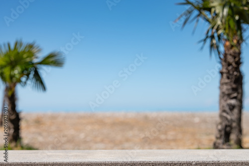 Concrete table surface with blurred palm trees, sea and  beach on background.