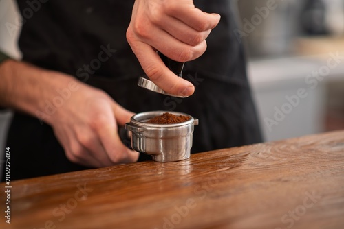 Εκτύπωση καμβά A close up of a barista pressing ground coffee with a metal tamper into a portaf