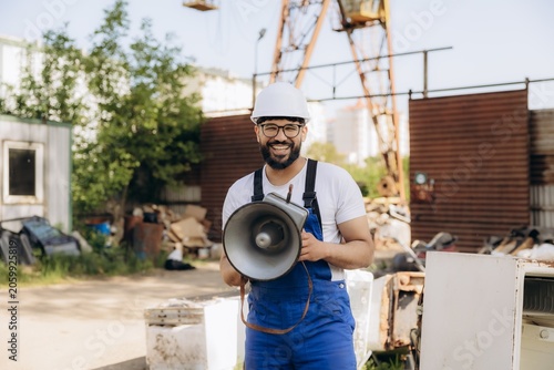 Fotografie Smiling worker holding megaphone in industrial scrapyard