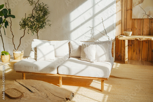 Obraz na plátně Sofa with pillows in sunny room with plants and natural wood desk, warm light