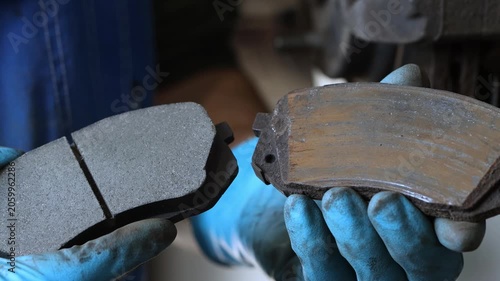 A car mechanic shows two car brake pads, an old one and a new one, close-up.