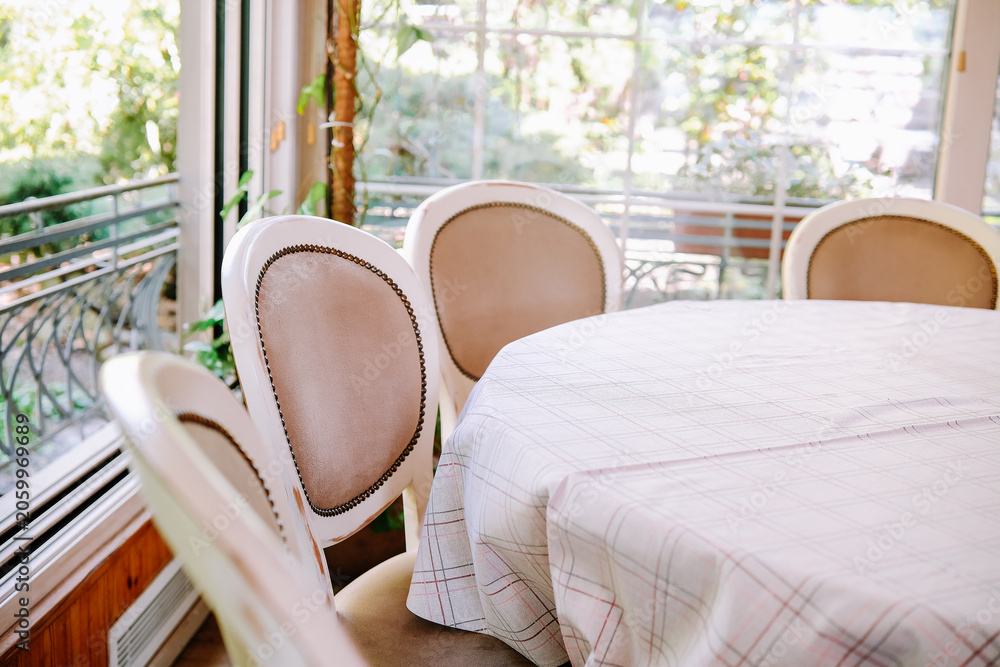 Obraz premium Dining chairs around a table with tablecloth near a window