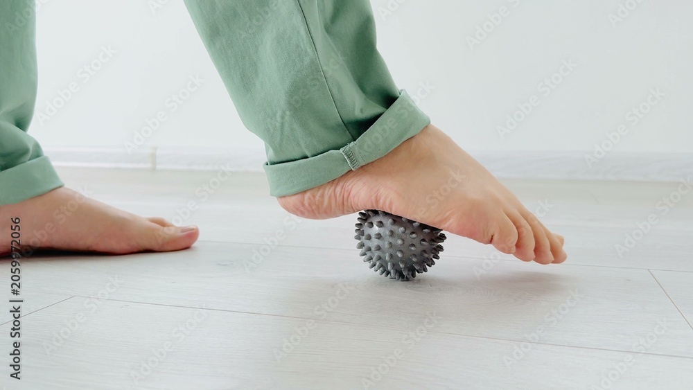 Fototapeta premium Textured foot roller ball being pressed on a bare foot over light wood flooring in a serene setting