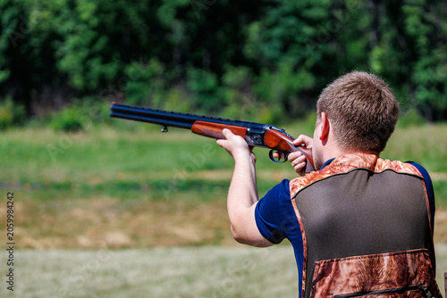 Young man aiming a double-barreled shotgun at a clay target shooting range, outdoor skeet and trap shooting sport