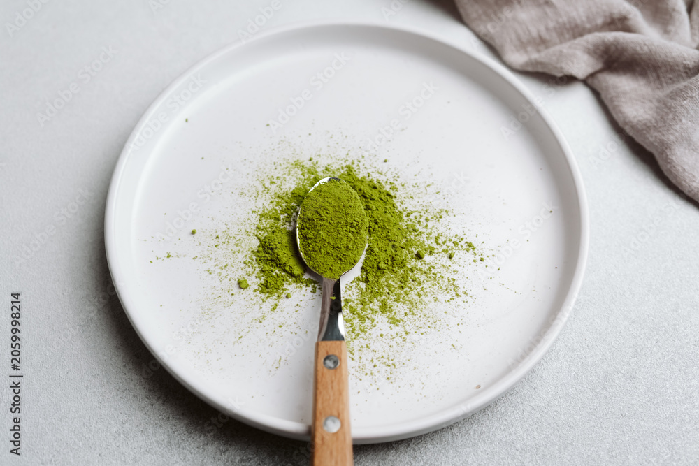 Obraz premium Green matcha powder on a spoon over a white plate