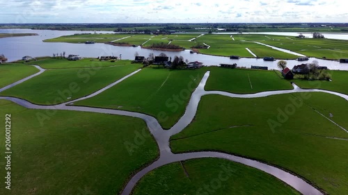 Aerial view of green rectangular fields divided by narrow water channels with scattered houses, farm buildings and distant lakes under partly cloudy sky in rural landscape