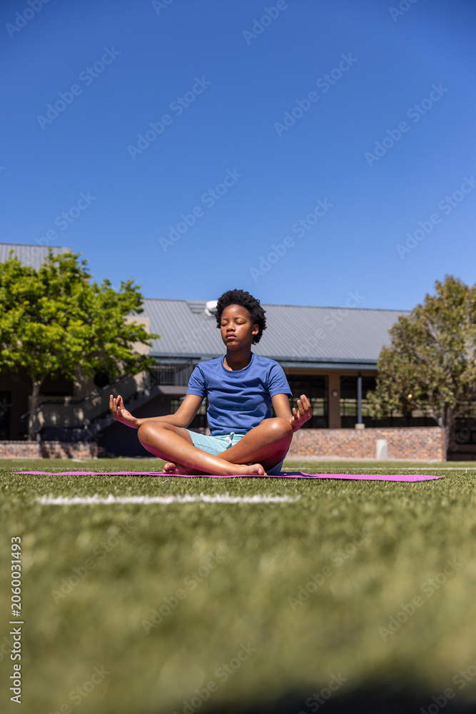 Obraz premium African American teen meditating on pink yoga mat on campus field, wearing blue T-shirt and shorts
