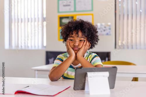 Schilderij op canvas African American school-age boy leaning at classroom desk, looking at tablet on