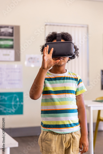 African American child adjusting VR headset in classroom near desk and board, striped shirt