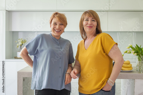 Smiling women enjoy time together in a modern kitchen during daylight hours with fresh fruit around them