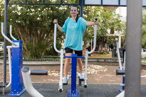 Cheerful woman exercising on outdoor fitness equipment in outdoor gym