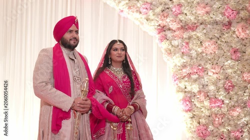 Traditional Sikh Bride and Groom Standing on Reception Stage with Floral Background