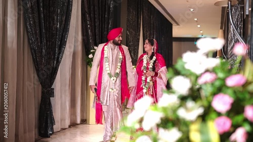 Happy Sikh Bride And Groom Walking Through Luxury Hotel Corridor With Foreground Flowers