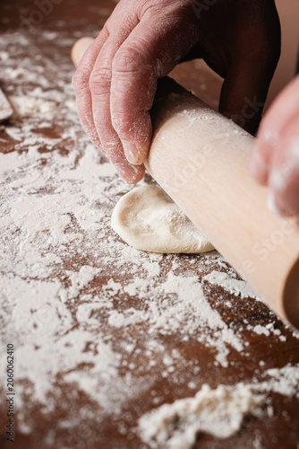 Obraz na plátně Hands using rolling pin to flatten dough on floured wooden table during homemade