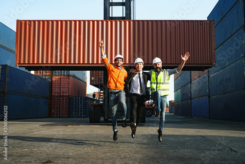 фотографія Three jubilant individuals leap with excitement amidst colossal stack of shippin
