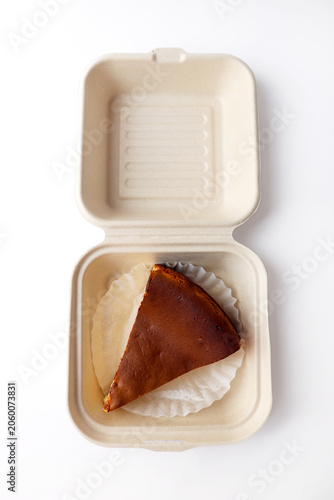 Slice of Basque Burnt Cheesecake in Takeout Container on White Background
