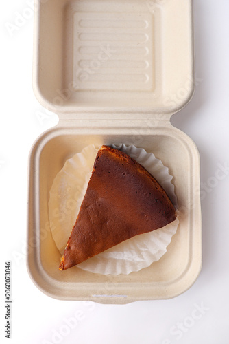 Slice of Basque Burnt Cheesecake in Takeout Container on White Background