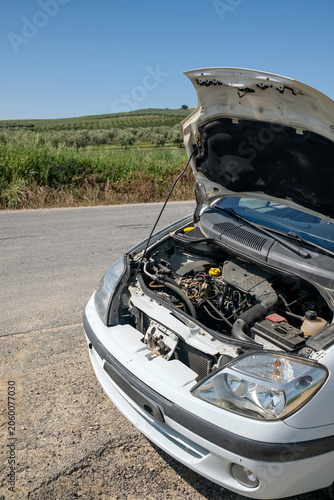 Bild auf Leinwand White car experiencing a breakdown on a rural roadside with its hood open, revea