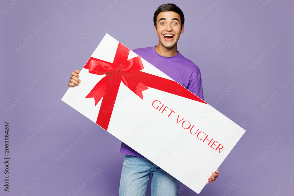 Fototapeta premium Young surprised shocked man he wears lavender t-shirt casual clothes hold gift certificate coupon voucher card for store isolated on plain pastel purple background studio portrait. Lifestyle concept.