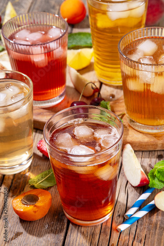 Summer refreshing drink, non alcohol tea based cocktails, iced tea varieties in different glasses, with fruit juices - strawberry, peach, apricot, cherry cold tea on wooden cozy background