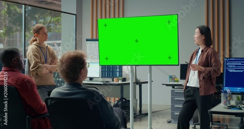 Office Meeting Presentation: Asian Woman Presenter Briefs Software Team in Office, Pointing to Large Green Screen Chroma Key Display. Engineering Ecommerce Platform, Video Game Development Meeting