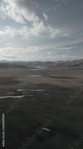 Vertical aerial shot of drone flying forward over spring mountain steppe valley against snowy peaks. Smartphone 916 aspect ratio. RAW flat profile uncorrected video footage.