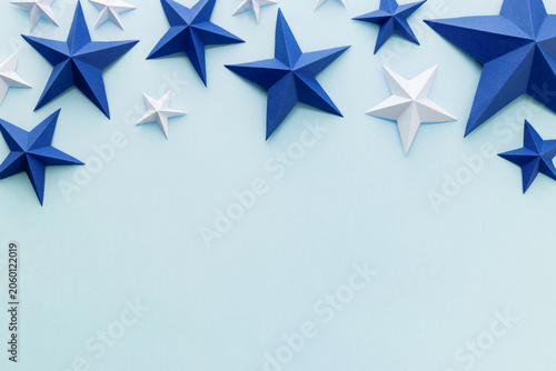 Minimal flat lay composition with blue and white origami paper stars on a light blue background with copy space. Festive handmade patriotic decoration for Independence, Memorial, Veterans or Flag day