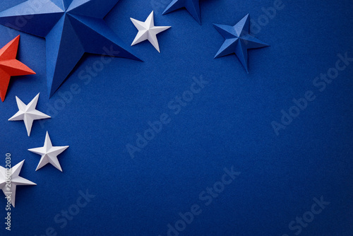 Festive arrangement of red, white and blue paper stars and curled ribbons on dark blue background. Patriotic border with empty space for text, suitable for Independence, Fourth of July, Memorial