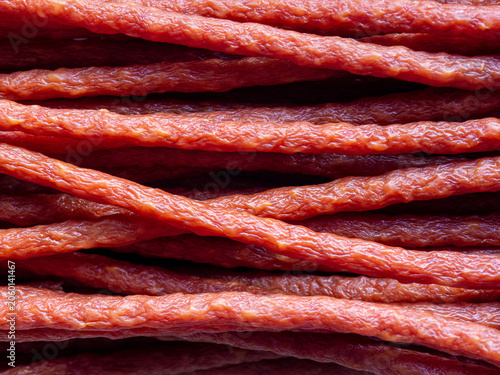 Close-up background of stacked kabanos sausage sticks with rich red color and detailed texture. Traditional dried and smoked meat snack arranged in layers, creating an abstract food pattern