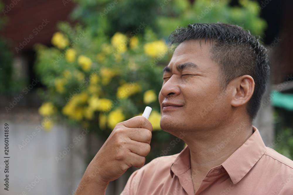Fototapeta premium Close-up of a man inhaling a herbal inhaler outdoors with eyes closed, enjoying a refreshing sensation, concept of traditional wellness, natural remedy, relaxation and self care