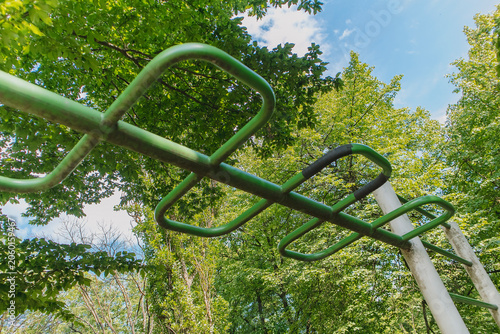 Photography Low angle view of outdoor monkey bars surrounded by green trees in a park, designed for fitness training and playground exercise