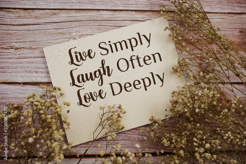 Live Laugh Love text written on paper card with flowers decorations on wooden background