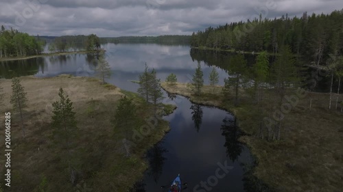 Aerial view of a person kayaking on a calm wilderness lake surrounded by pristine taiga forest and marshland in Mujejärvi, Finland.