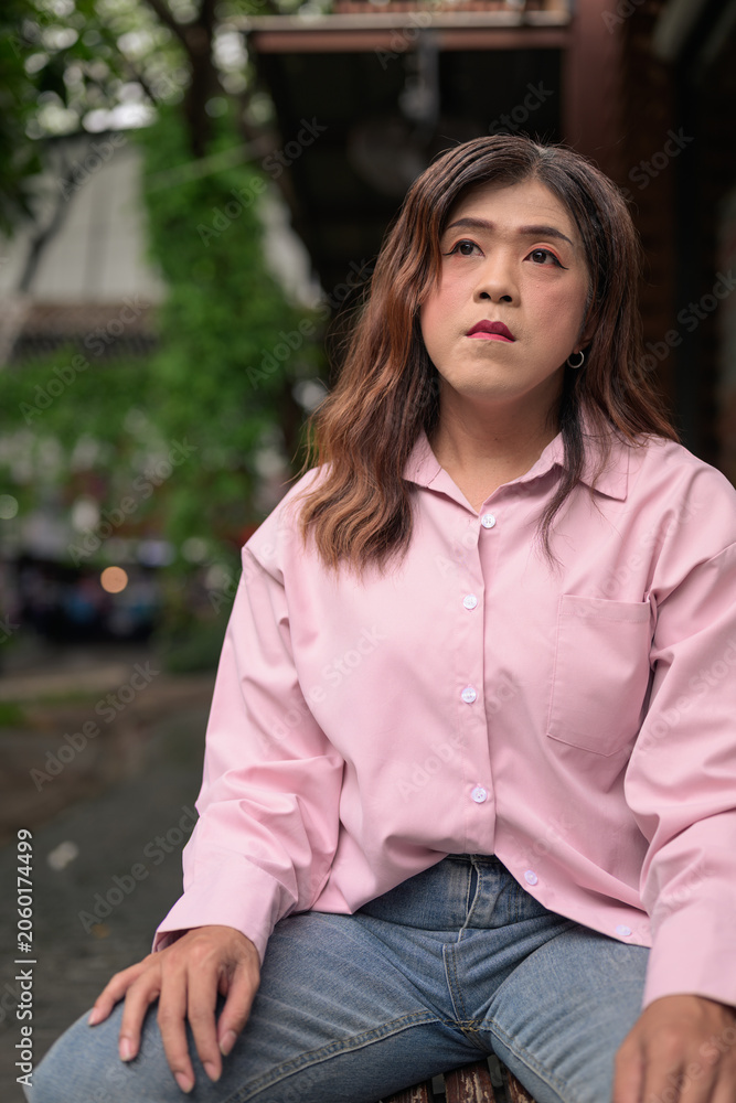 Naklejka premium Transgender Thai Isan woman looking away thoughtfully while sitting on an outdoor bench