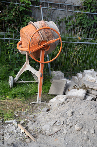 Quadro em tela Orange concrete mixer beside cinderblock pile in backyard construction site