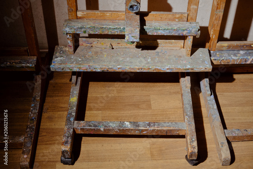 Artist's easel covered in colorful paint splatters. Shallow depth of field