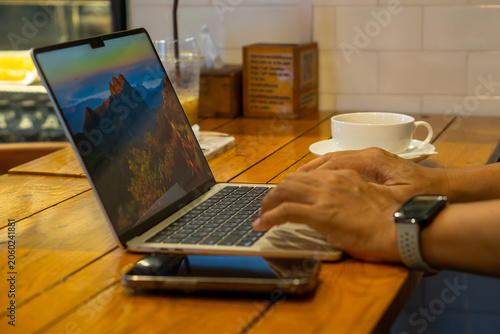 Businessman working on laptop with mountain scenery on screen in cafe.