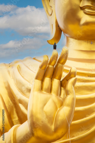 Canvastavla Bird Perched on Giant Golden Buddha Statue Finger,A tiny bird sitting on the fingertip of a colossal golden Buddha statue hand against a blue sky with clouds