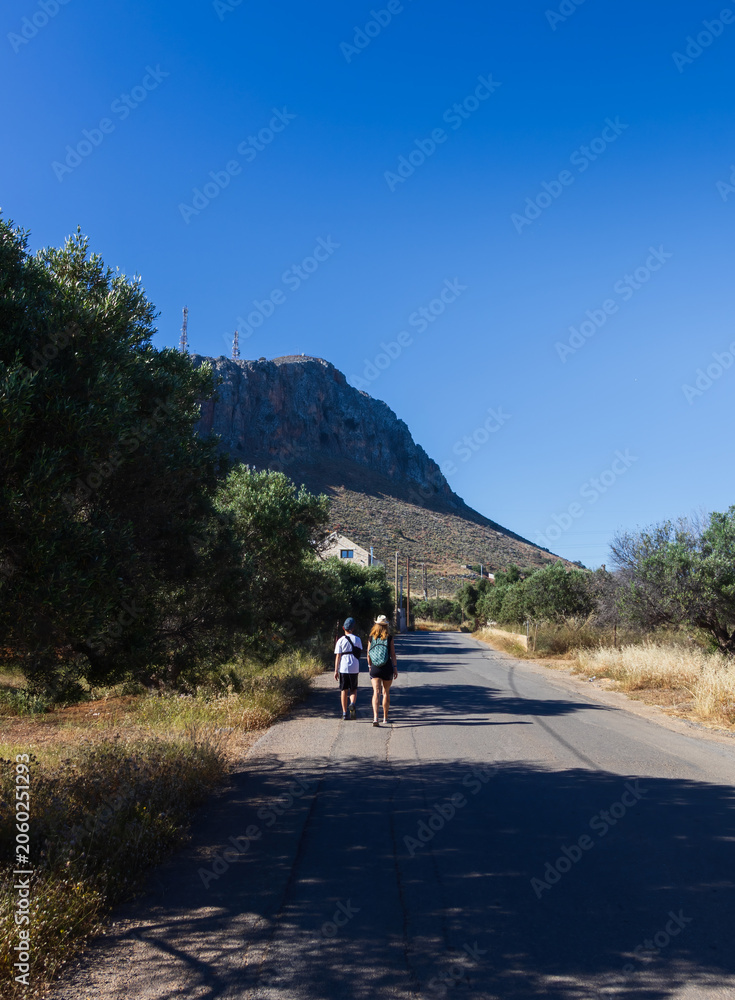Obraz premium Mother and young son with an arm brace walking on a road towards Gouves village in Crete. Mount Ederi in the background, enjoying a vacation despite medical restrictions